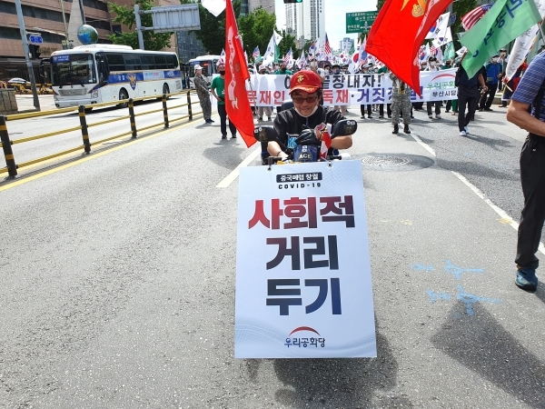 지난 달 25일 서울 중구 을지로 일대에서 열린 우리공화당 집회에서 한 당원이 사회적 거리 두기 안내표지판을 들고 행진하고 있다.