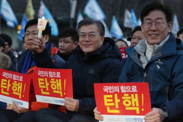지난 2017년 초 광화문 촛불집회에 참석한 안희정, 문재인, 이재명이 박근혜 대통령 탄핵 피켓을 들고 웃고 있다.